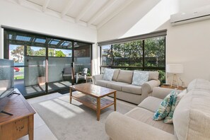 Una sala de estar moderna con un sofá, una mesita de centro y un ventanal de vidrio que da a un espacio exterior.