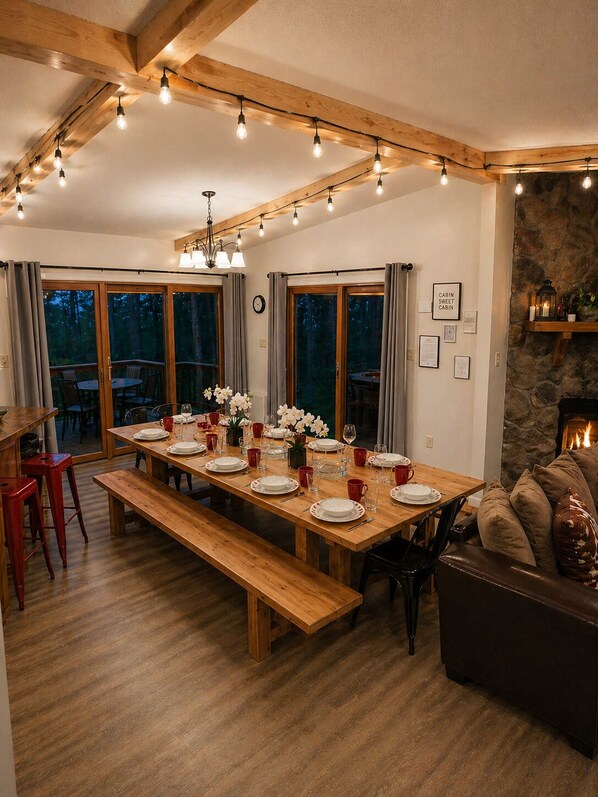A dining area with a long wooden table set for six, benches, and a stone fireplace.