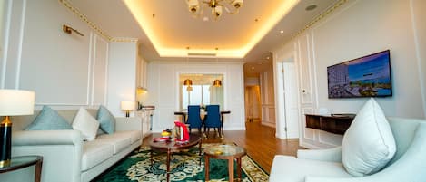 A spacious living room with a white sofa set, a green patterned rug, and a chandelier.