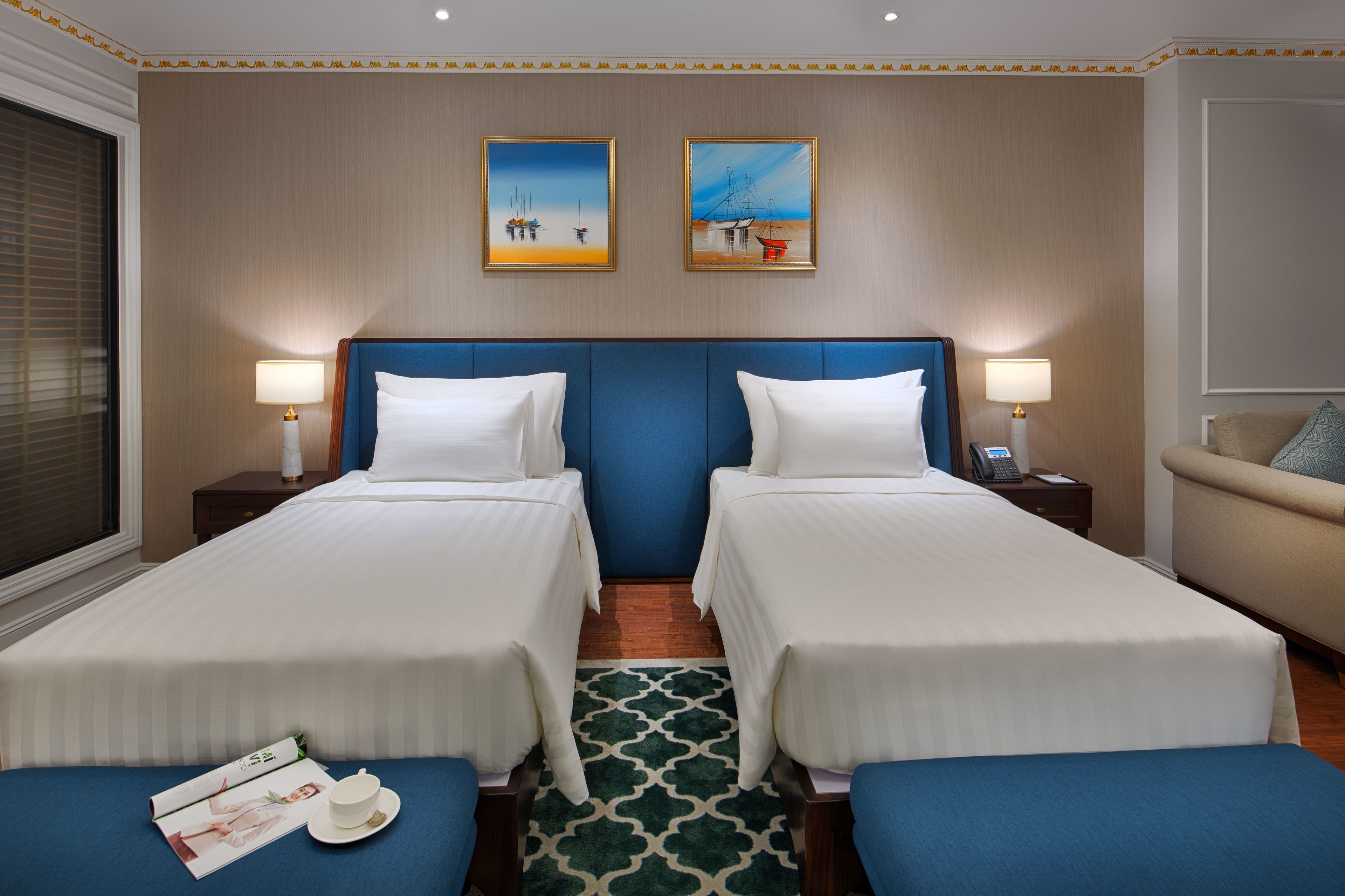 A hotel room with two single beds, a sofa, a small table, and two paintings on the wall.
