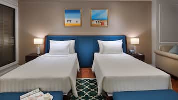 A hotel room with two single beds, a sofa, a small table, and two paintings on the wall.