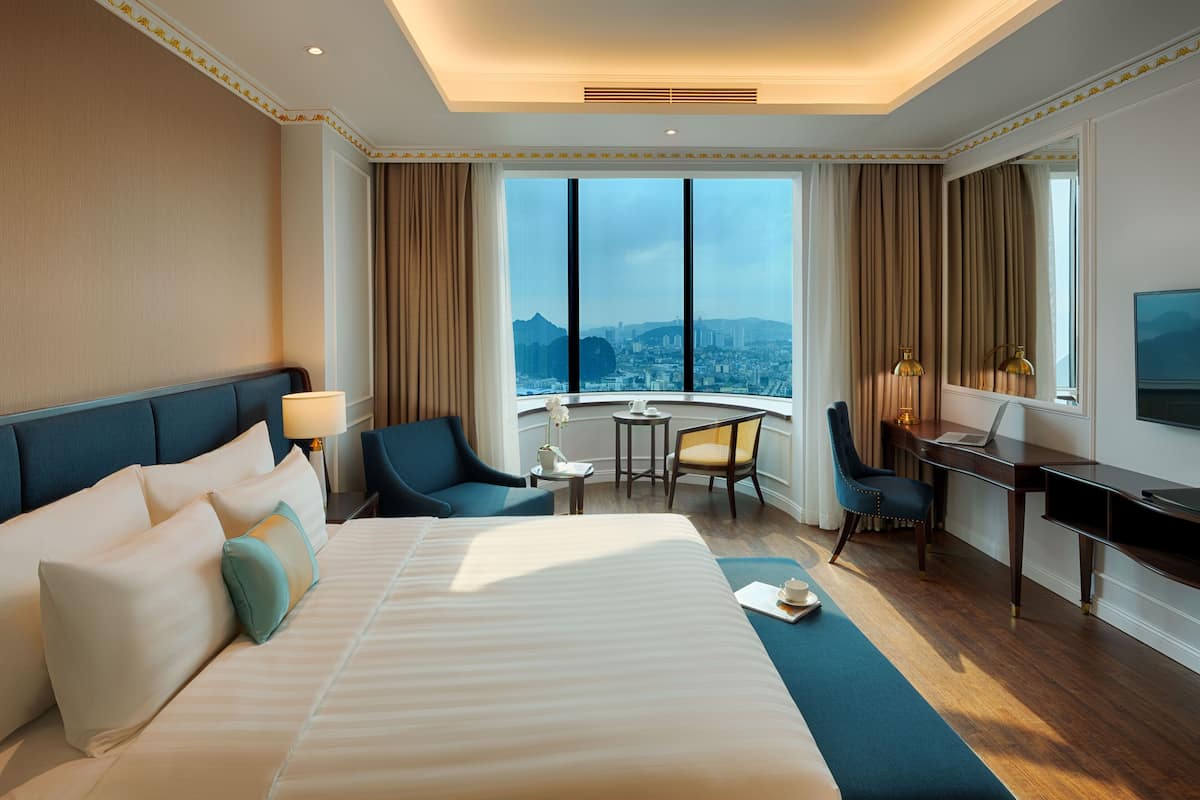 Ein Hotelzimmer mit einem großen Bett, einem Schreibtisch, einem Sessel und Blick auf die Stadt.