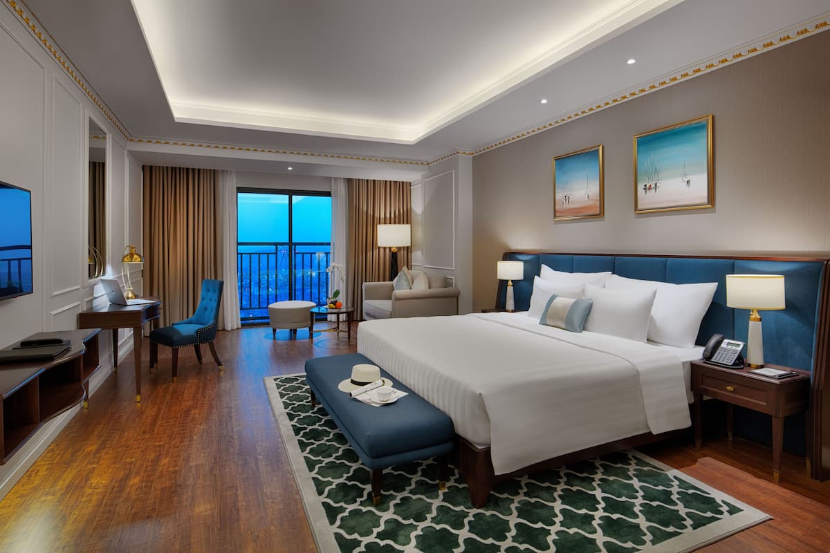 Ein Hotelzimmer mit einem großen Bett, einem Schreibtisch, einem Stuhl, einem Balkon mit Blick und zwei Bildern an der Wand.