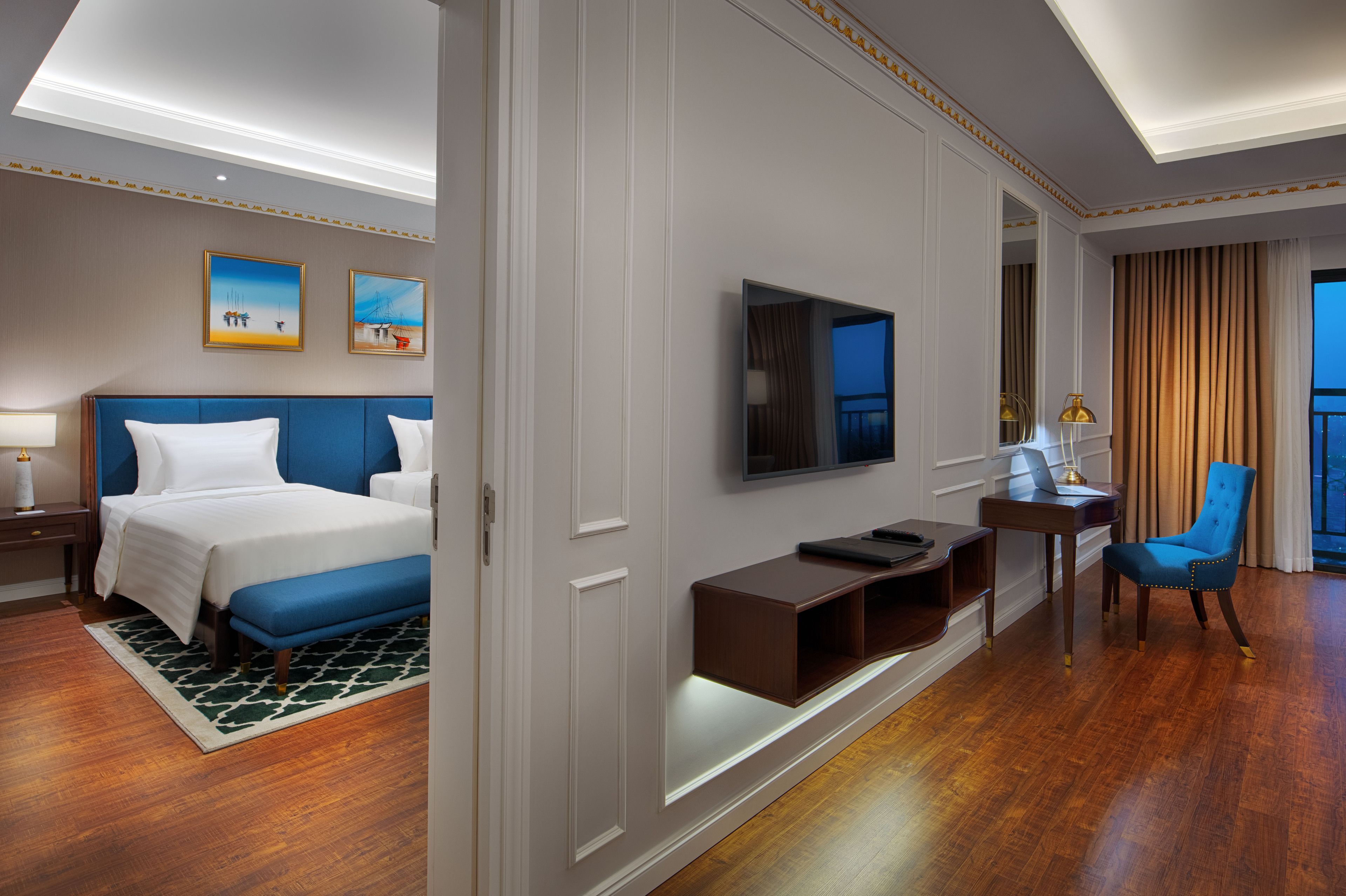 A hotel room with a large bed, a desk with a laptop, a TV, and a chair.