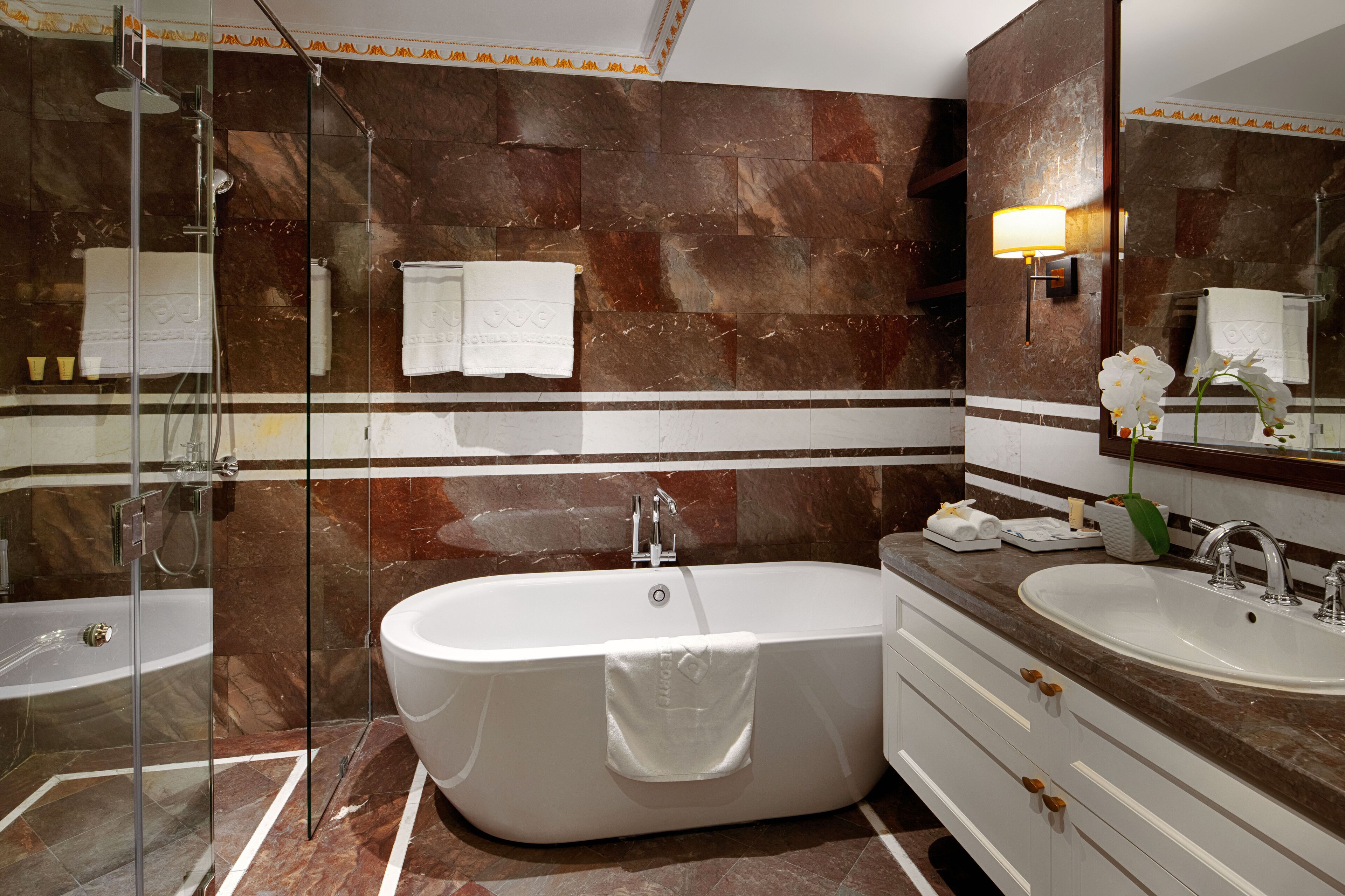 Une salle de bain moderne avec une baignoire sur pieds, deux vasques, une douche à l’italienne et des murs en marbre.