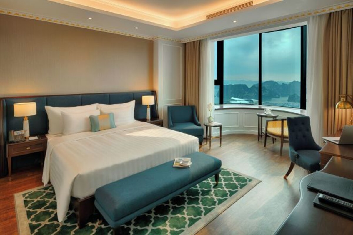 A hotel room with a large bed, a desk, a chair, and a view of the mountains.