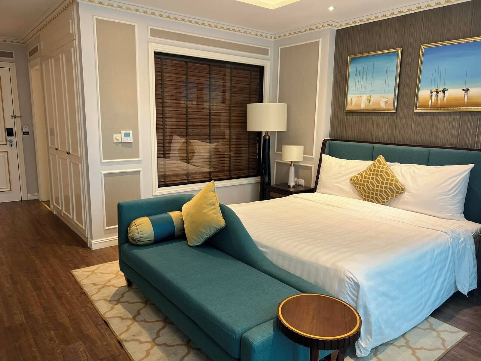 A bedroom with a large bed, a sofa, a round side table, and a window with blinds.
