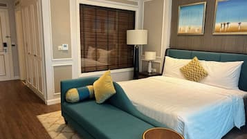 A bedroom with a large bed, a sofa, a round side table, and a window with blinds.
