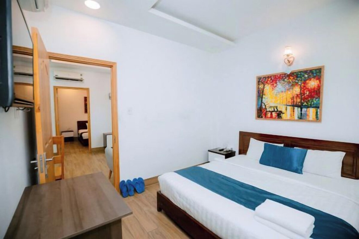 A hotel room with a bed, a desk, and a painting on the wall.