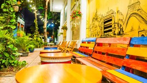 Un café con mesas y bancos de madera, plantas en macetas y un mural de un monumento famoso.