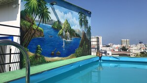 Una piscina con un mural de paisaje tropical, que incluye palmeras y una cascada.