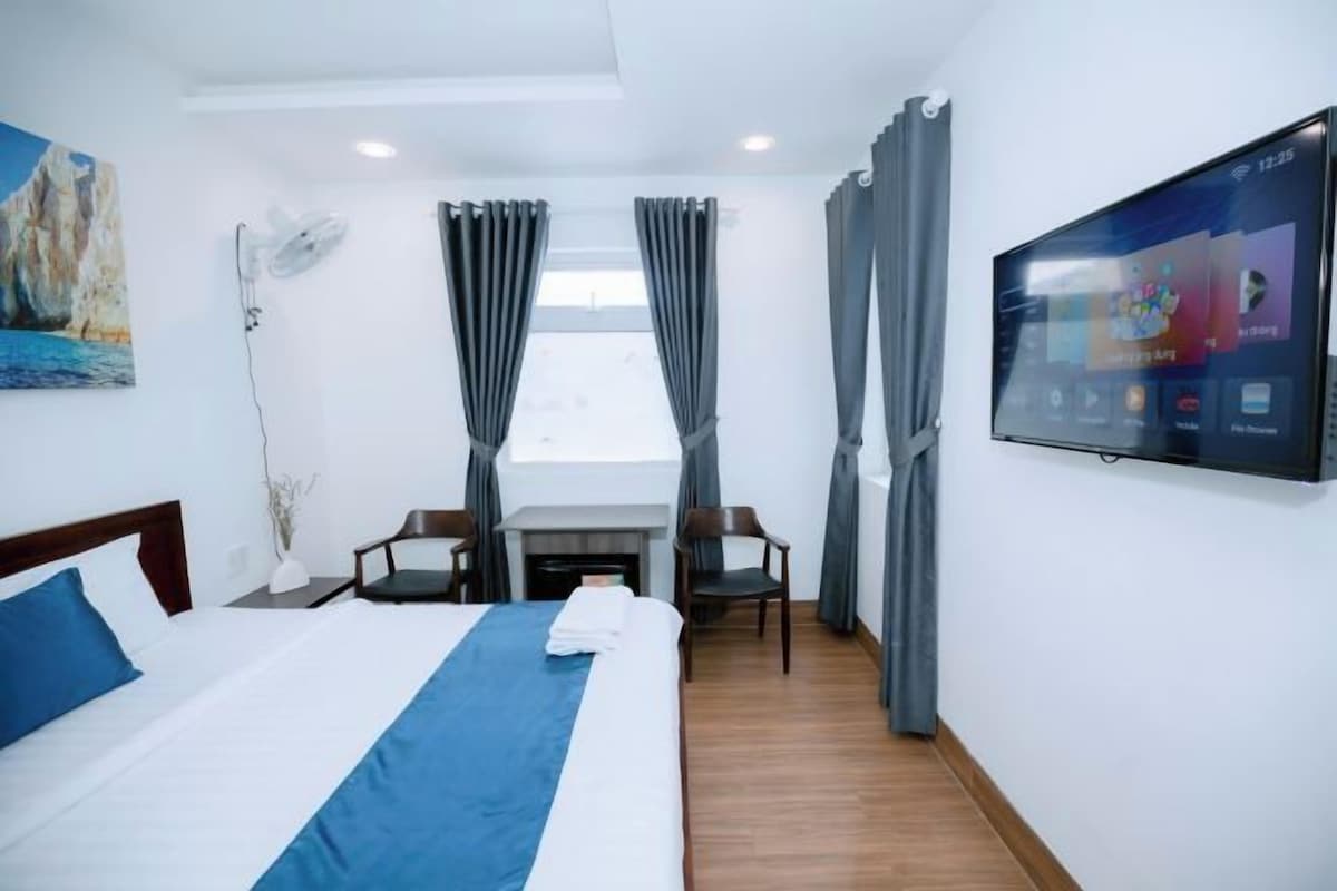 A hotel room with a bed, a desk, two chairs, a flat-screen TV, and a painting on the wall.