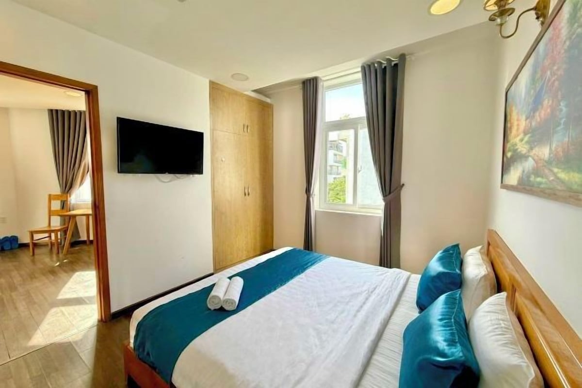 A hotel room with a bed, a television, a wardrobe, and a window with curtains.