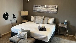 Un dormitorio con una cama grande, una mesita de noche, una lámpara, un cuadro en la pared y suelo con alfombra.