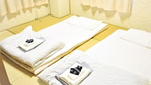 Two neatly made beds with white linens and towels, a wooden floor, and a window with curtains. - Business Ryokan Harada (Hiroshima)