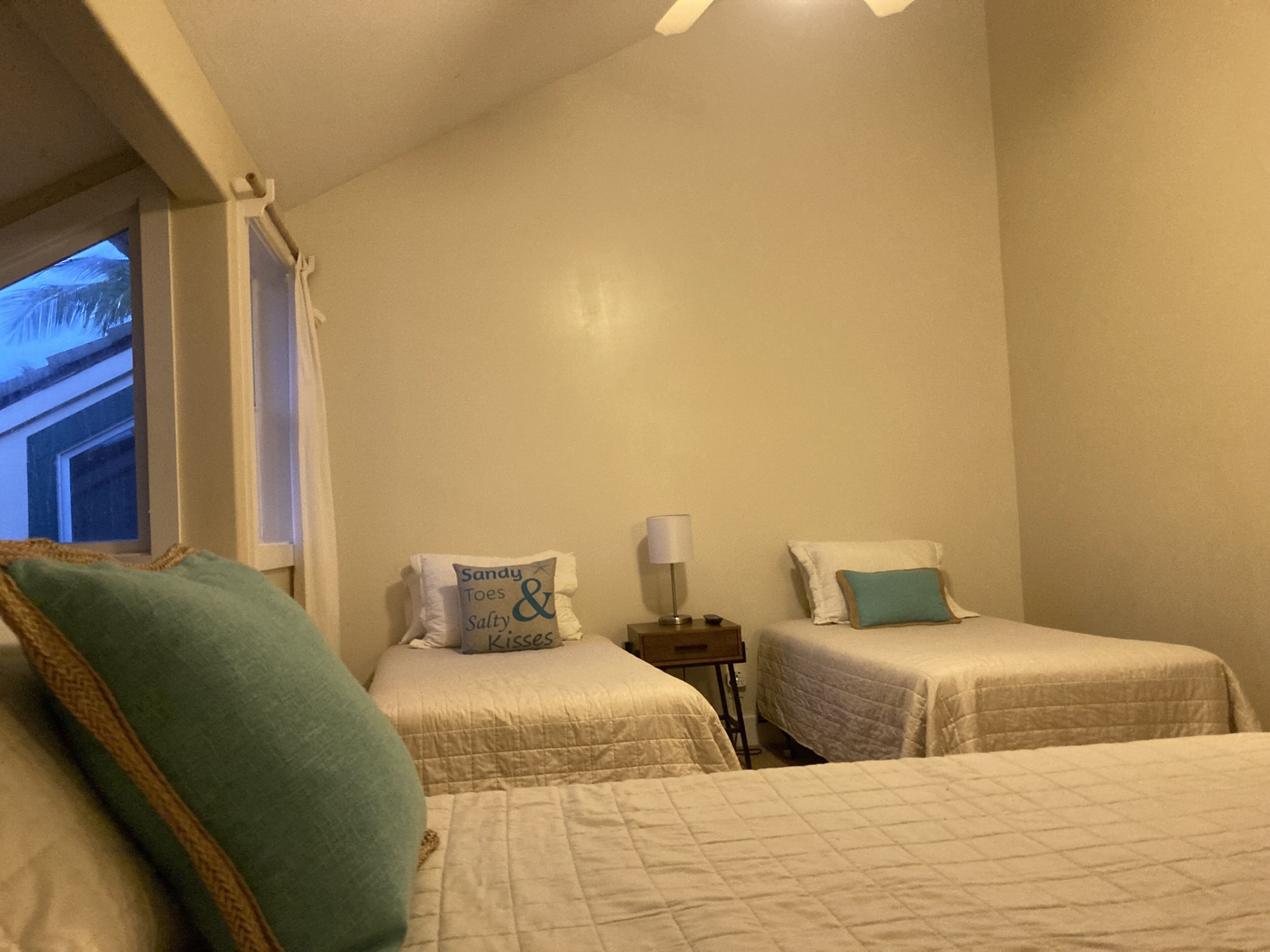 Quarto com duas camas de solteiro, mesa de cabeceira, abajur e janela com cortinas.