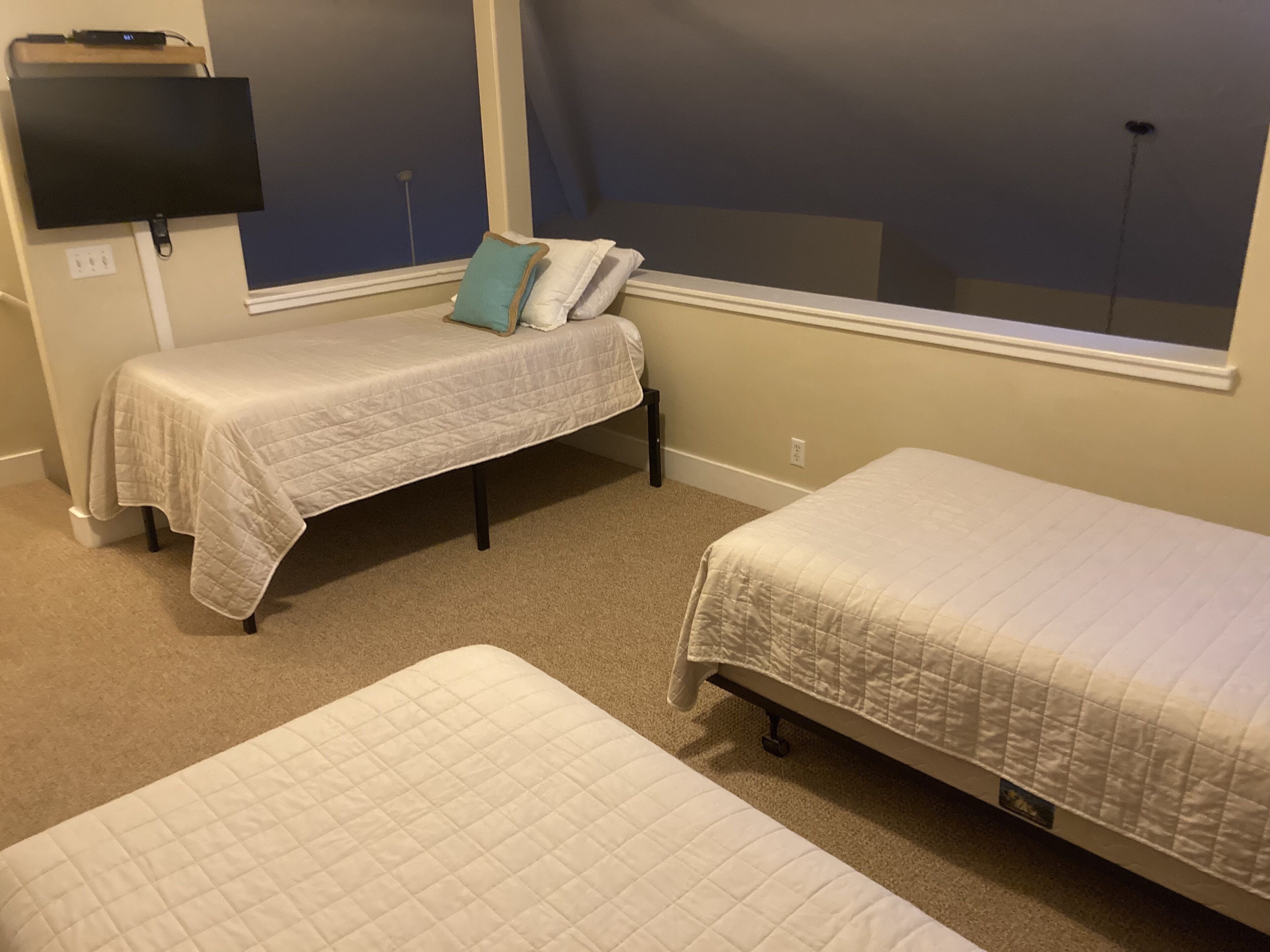 A room with two single beds, a TV mounted on the wall, and a window with a view of the sky.