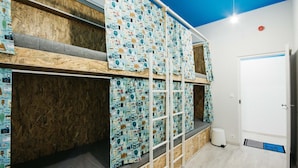A room with bunk beds covered in patterned fabric, a white door, and a vent on the floor. - Hello Hostel (Budapest)