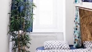 A room with a bunk bed, a potted plant, and a window with curtains. - Hello Hostel (Budapest)
