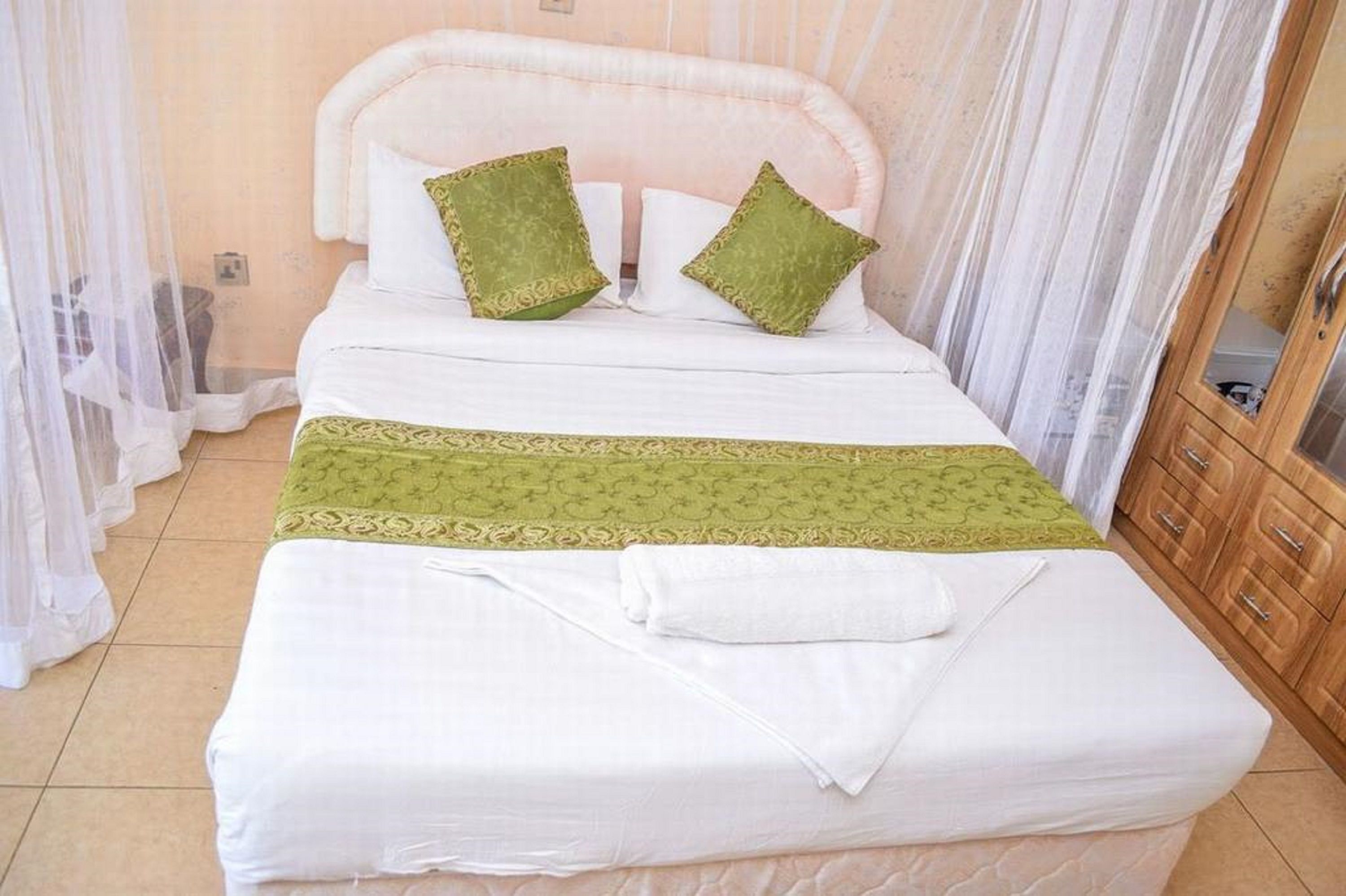 Un letto rifatto con lenzuola bianche, copriletto a motivi verdi e due cuscini verdi.