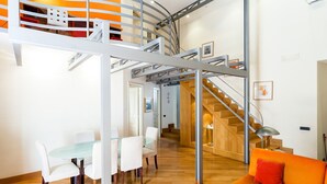 A modern interior with a glass dining table, white chairs, a wooden staircase, and an orange sofa. - Casa Rossella - My Rental Homes (Sorrento)