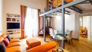 A modern living room with a large orange sofa, a flat-screen TV, and a dining area with a glass table. - Casa Rossella - My Rental Homes (Sorrento)