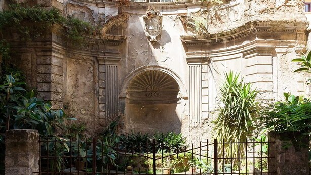 A historic stone building with arched windows and a central doorway, surrounded by a small garden and a metal fence. - Casa Rossella - My Rental Homes (Sorrento)