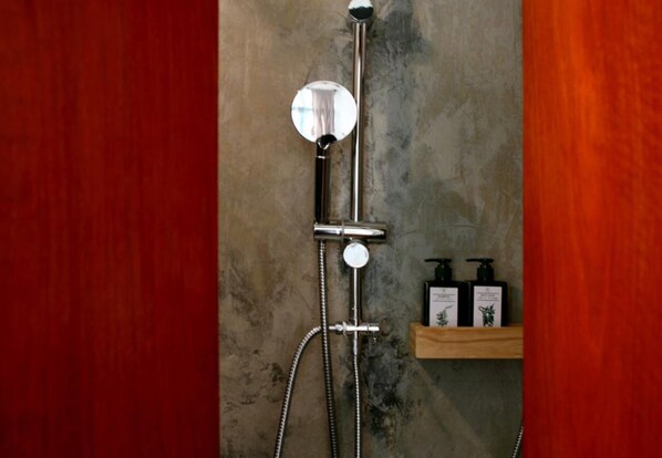 A shower with a handheld mirror, a handheld showerhead, and a handheld faucet. There is a wooden shelf with two bottles of shampoo and conditioner. - T-Boutique Hostel (Bangkok)