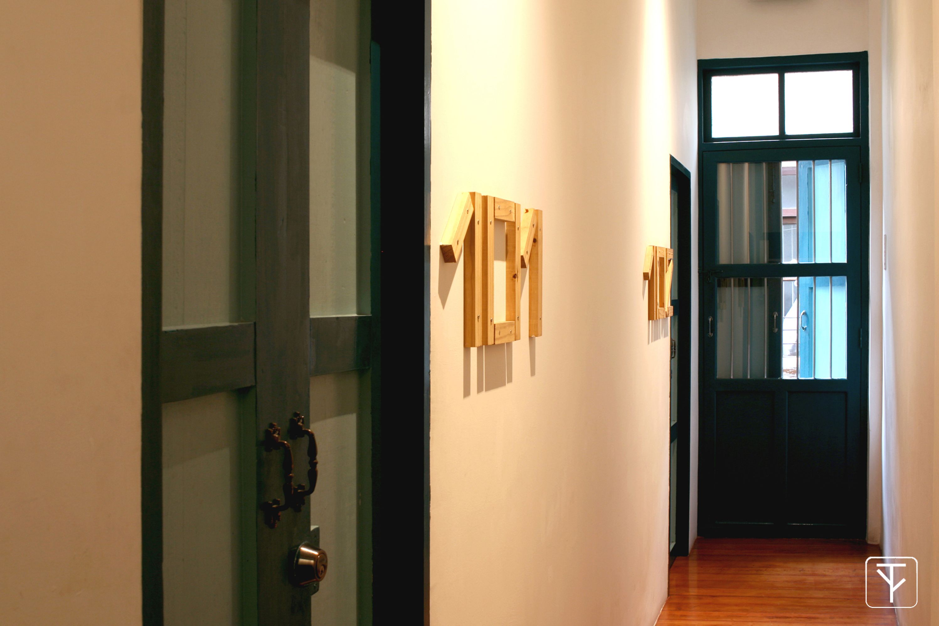 A hallway with a wooden door, a wall-mounted light fixture, and a door with a window.