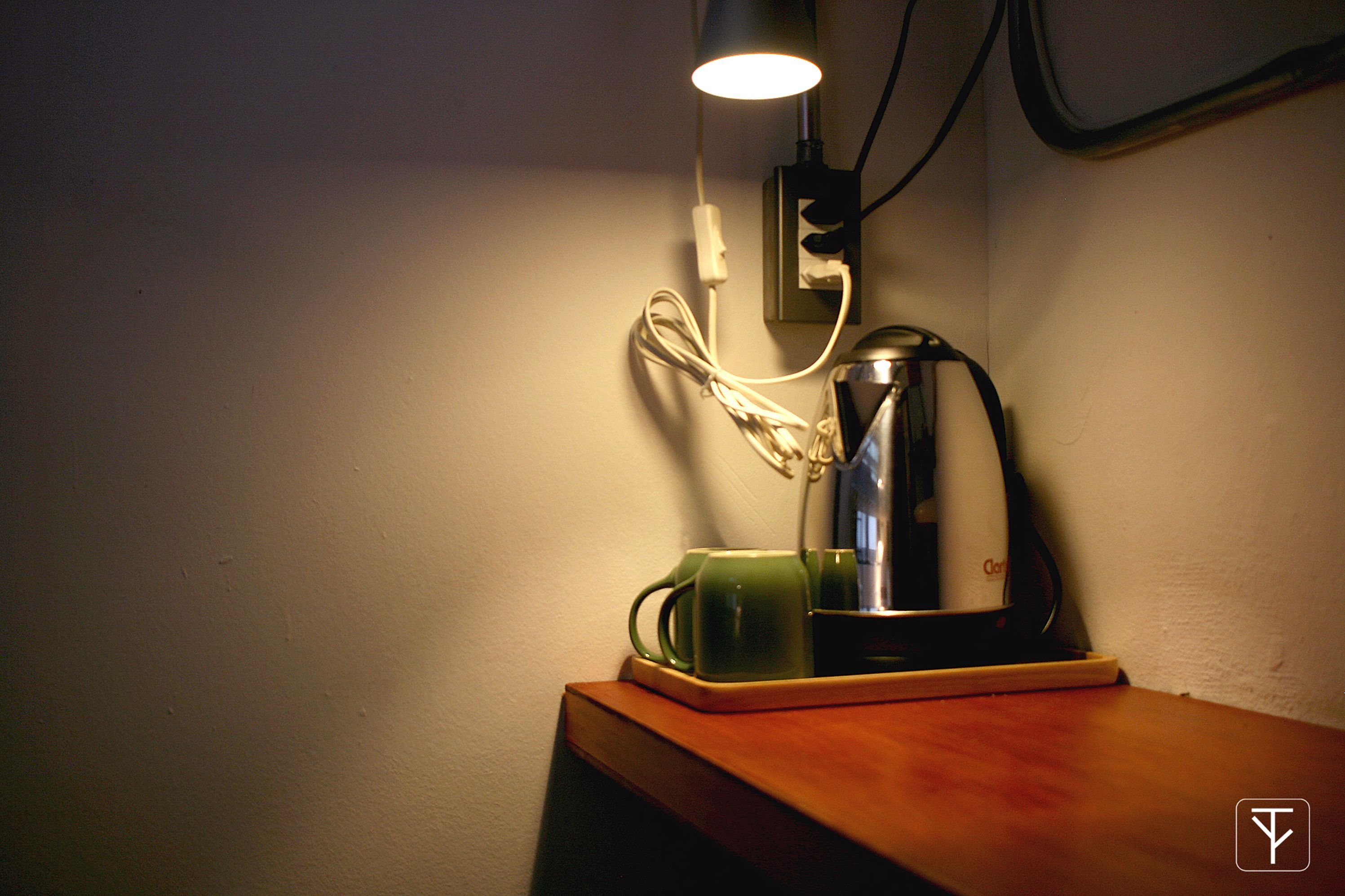 En skrivebordslampe med ledning, en grøn kop og en kaffemaskine på en træoverflade.