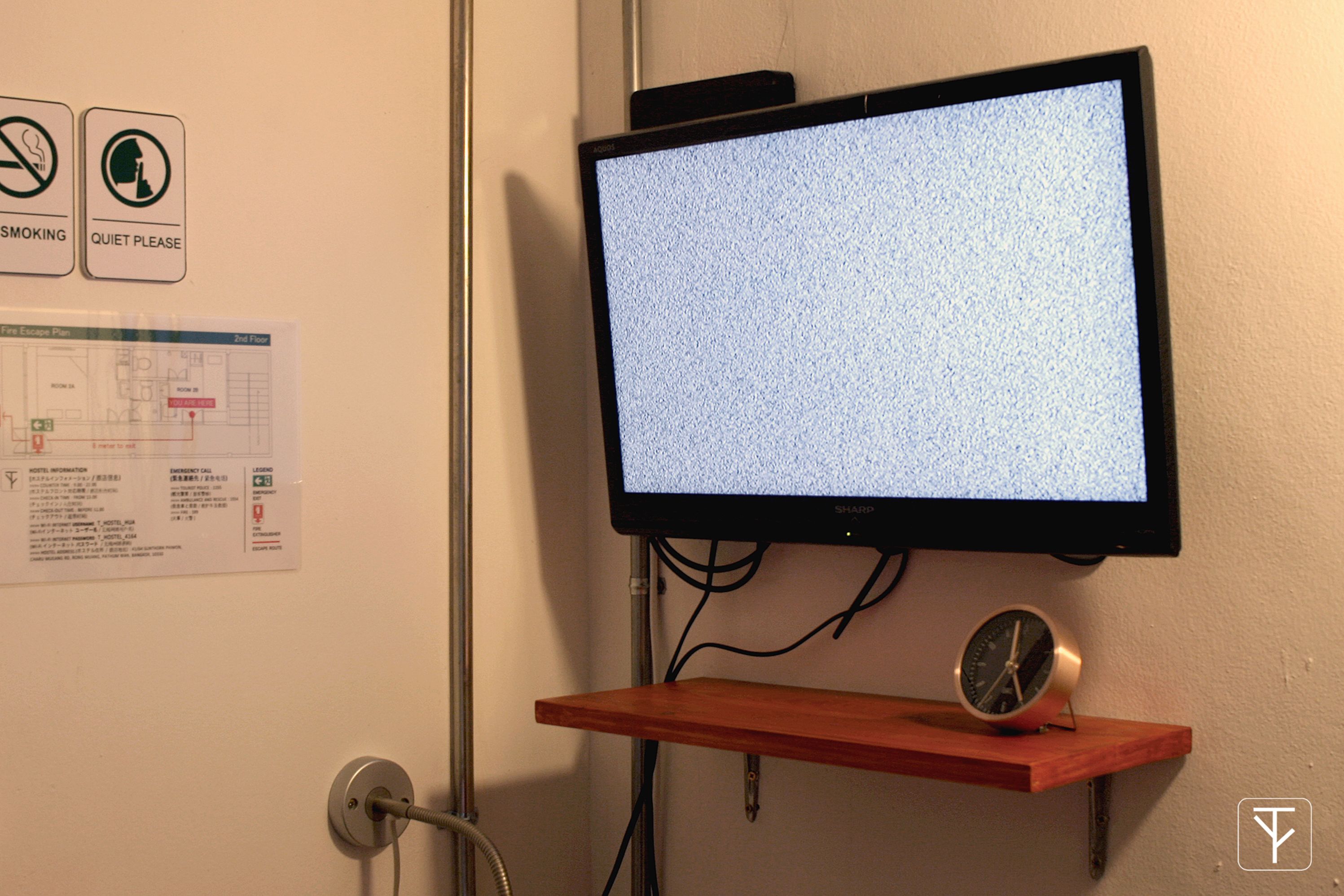 A wall-mounted TV, a fire exit plan, and a clock on a shelf.