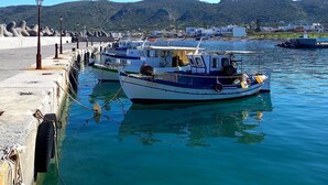 Un puerto con barcos amarrados, un muelle de hormigón y montañas al fondo.