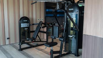 A gym with various exercise machines, a bench, and a wall-mounted rack.