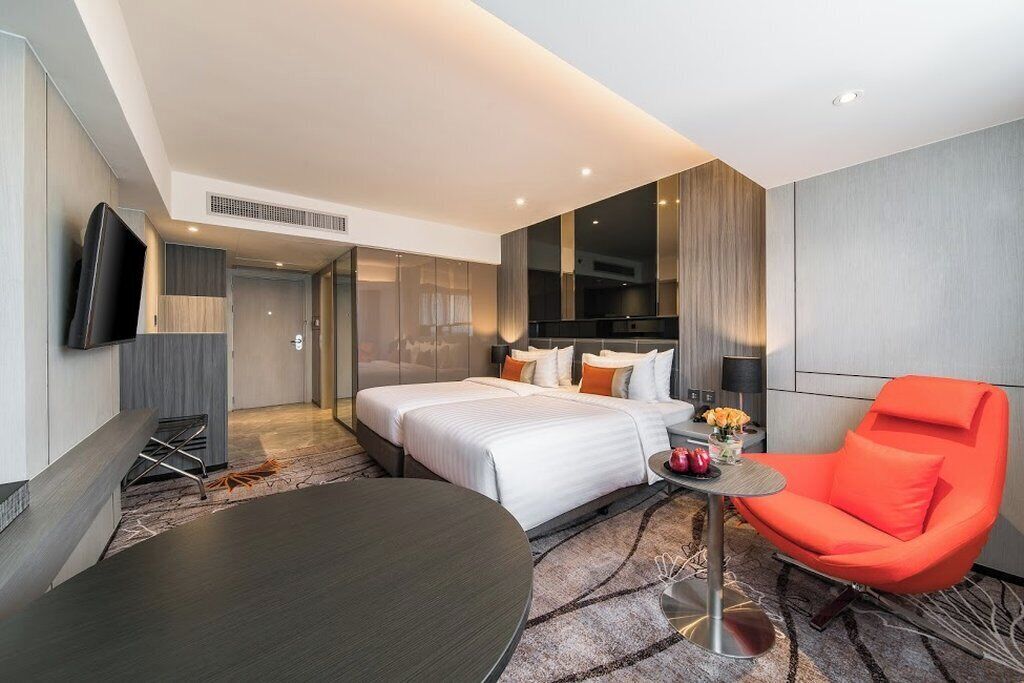 Een moderne hotelkamer met een groot bed, een ronde tafel, een feloranje stoel en een flatscreen televisie aan de muur.