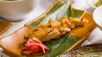 A plate of food with a green leaf, chicken, and a red garnish.
