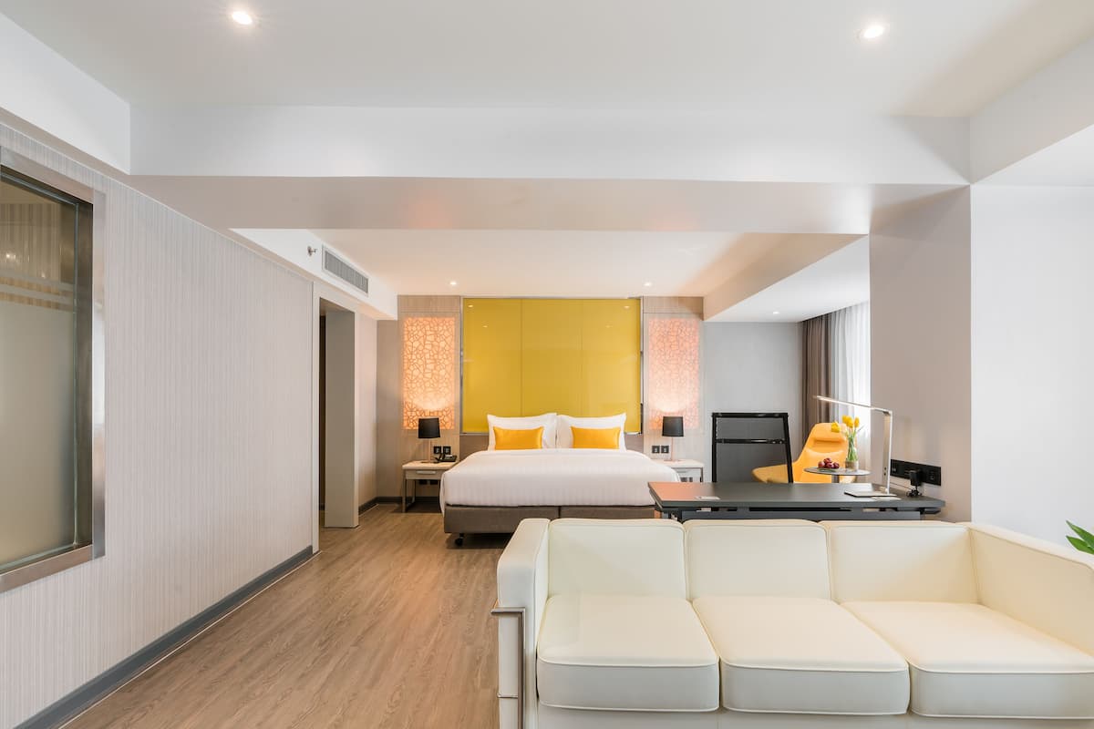 Ein modernes Hotelzimmer mit einem großen Bett, einem Schreibtisch mit Computer, einer Couch und einer Stehlampe.