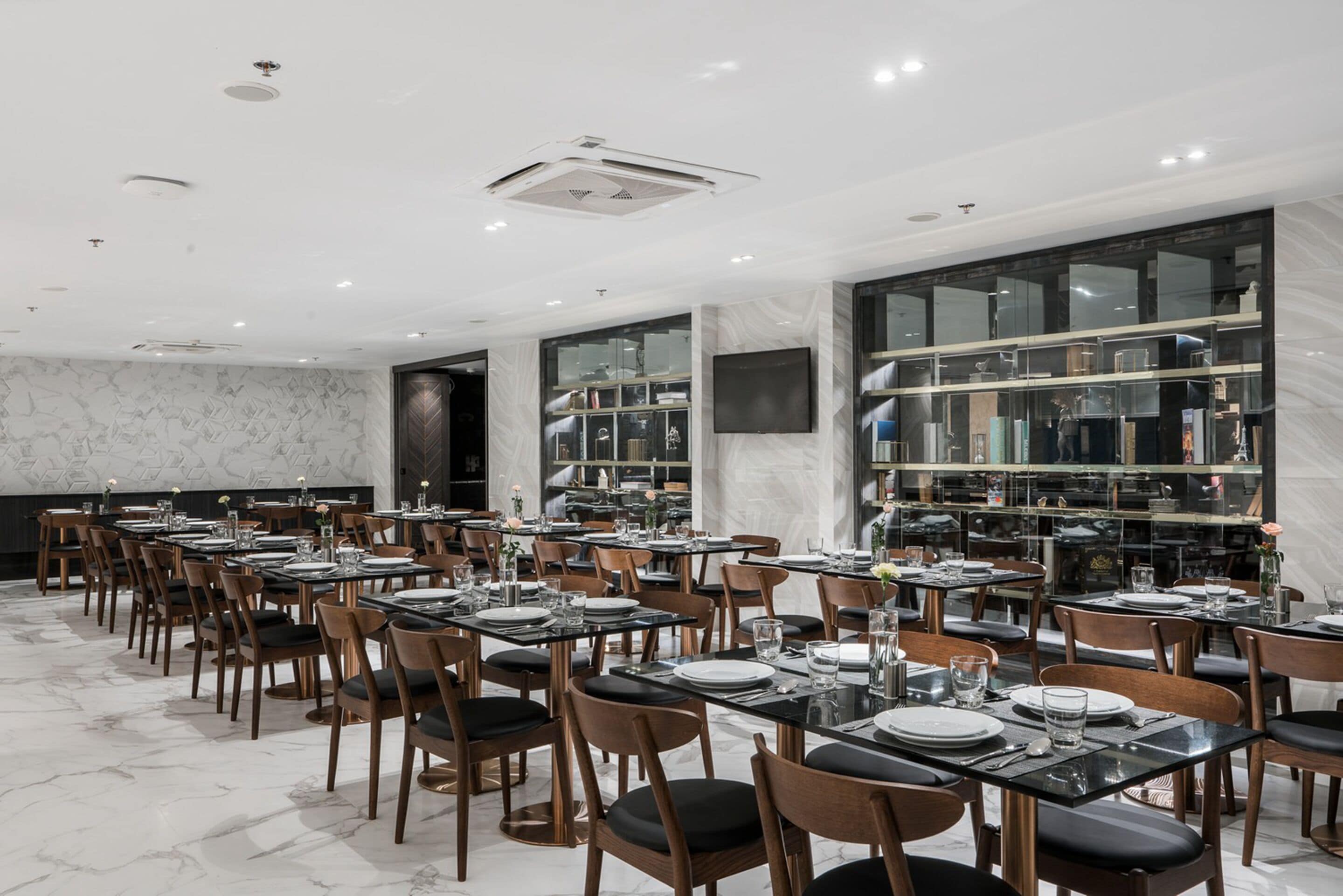 A modern dining area with marble flooring, wooden chairs, and tables set for a meal.