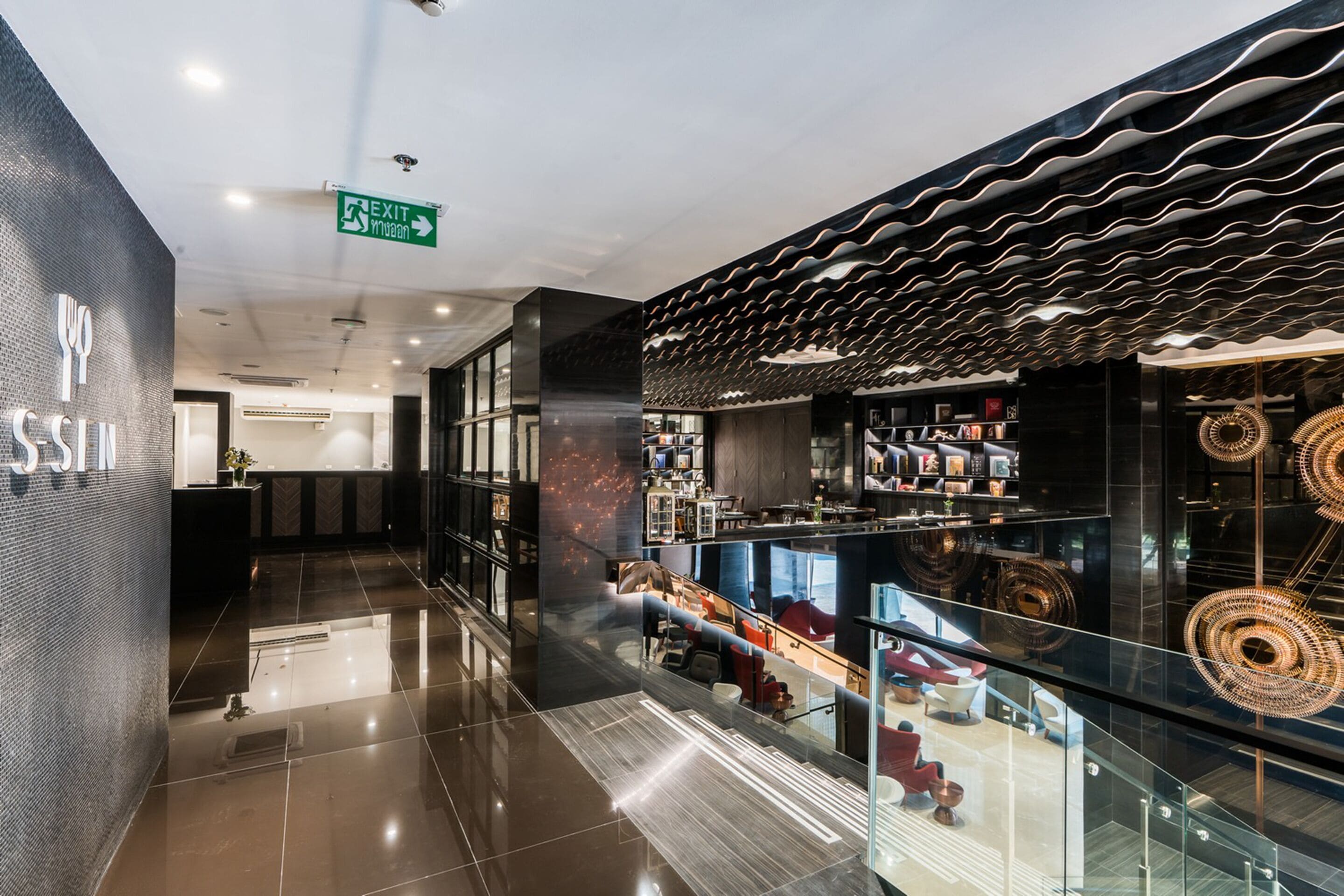 A modern hotel lobby with a reception desk, a staircase, and a glass railing overlooking a lower level.