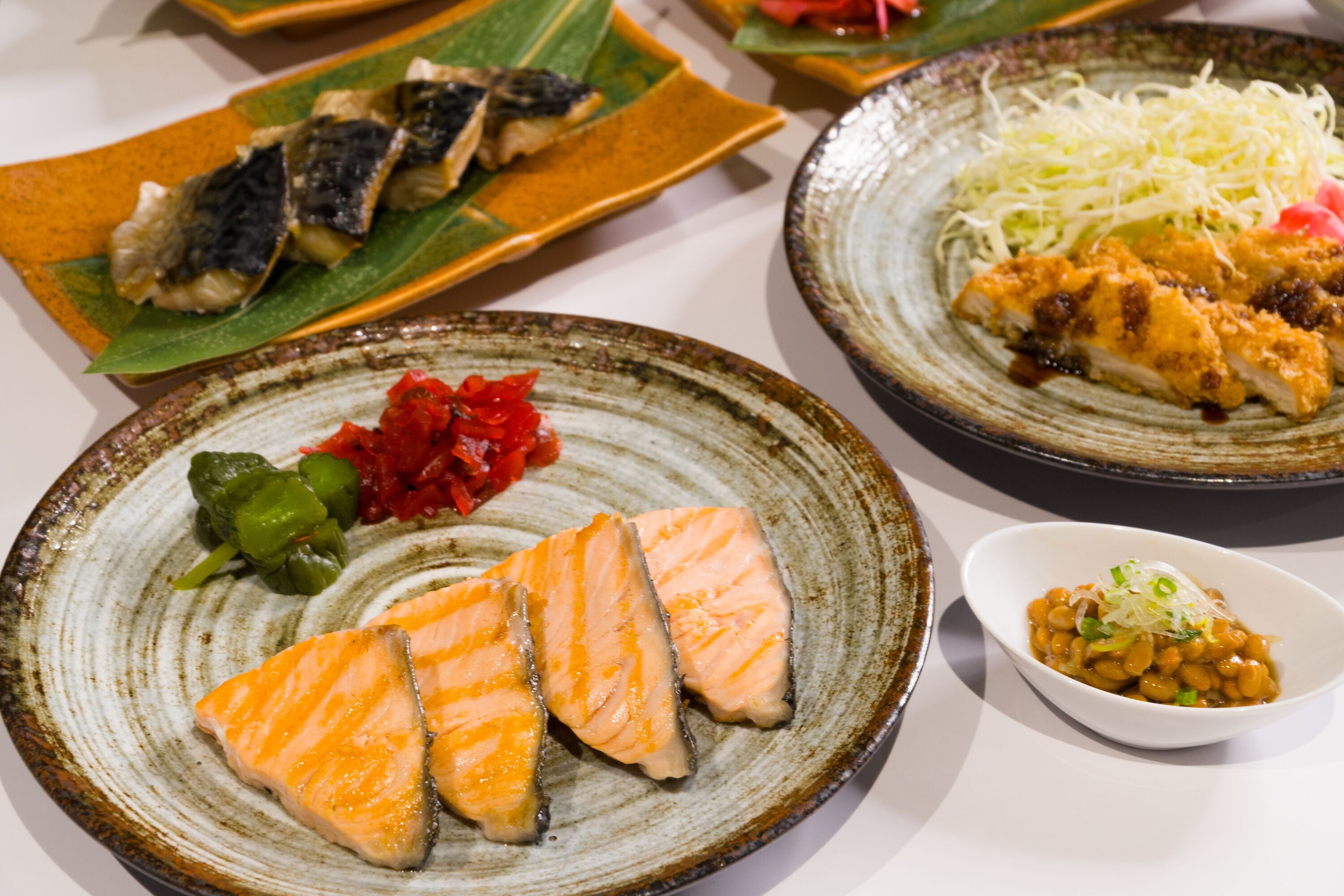 A variety of dishes on ceramic plates, including salmon, vegetables, and a bowl of beans.