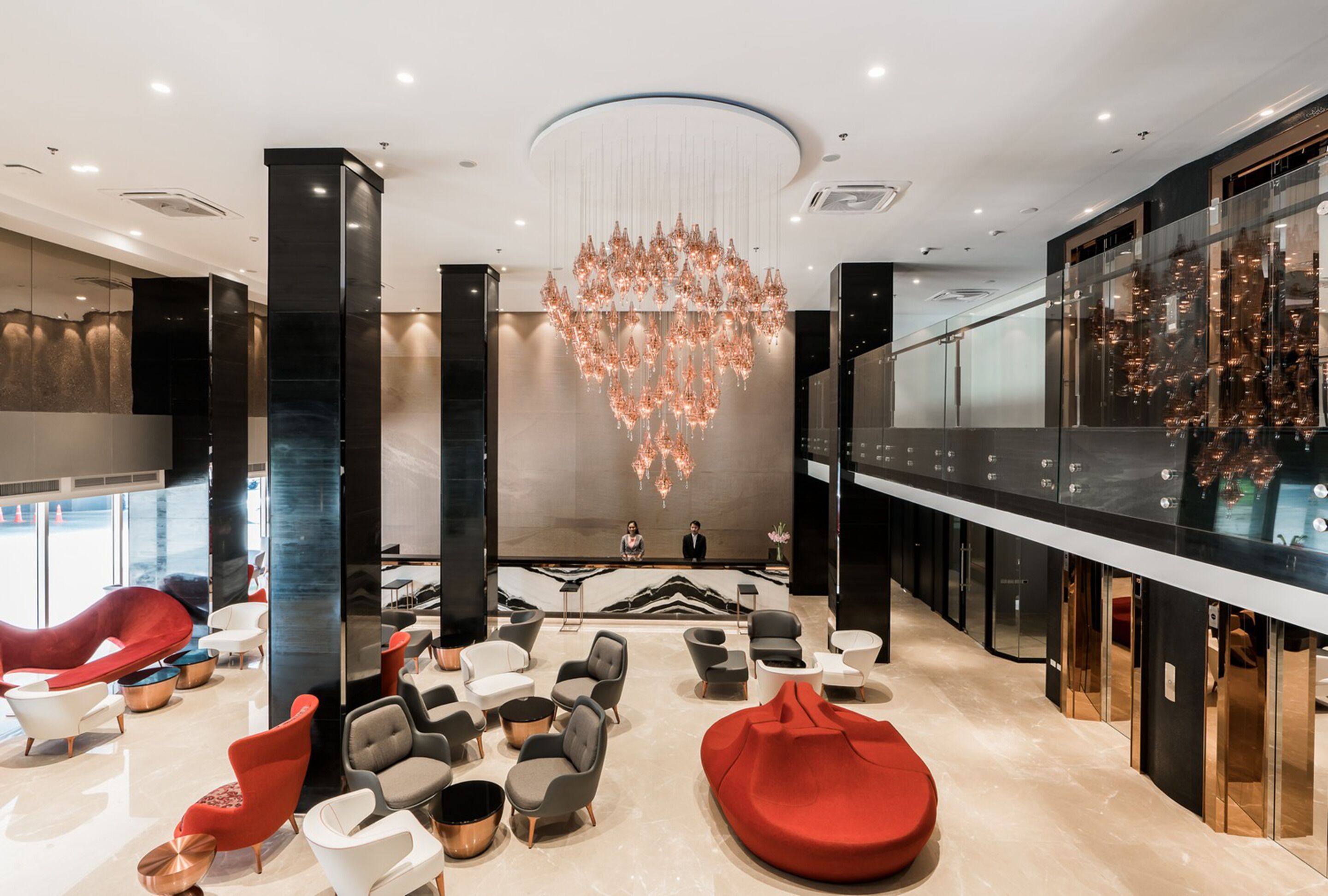 A modern lobby with a large chandelier, seating areas, and a reception desk.