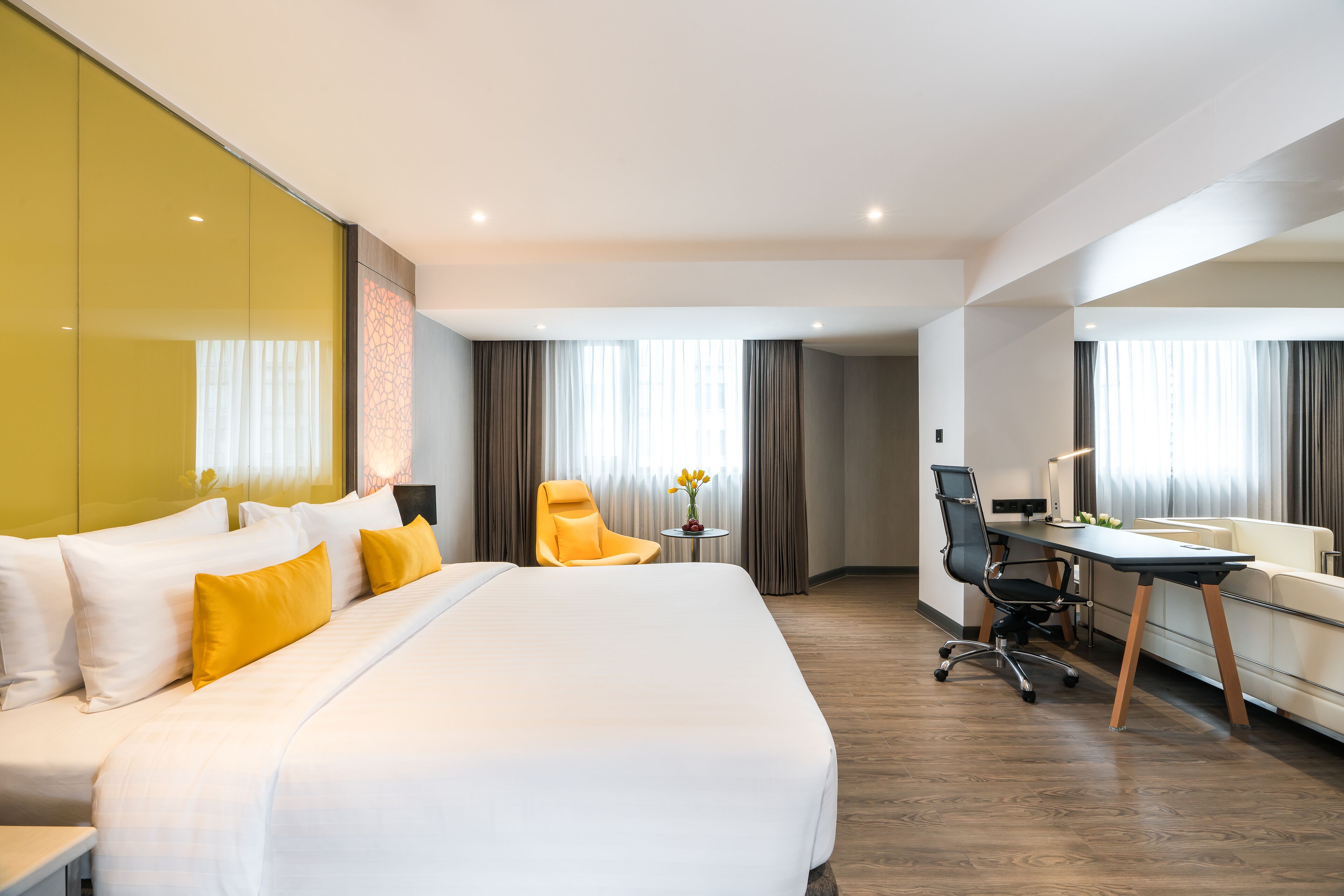 Een hotelkamer met een groot bed, een bureau, een stoel en een klein tafeltje met een bloevas.