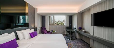 A hotel room with a large bed, a desk, a chair, a TV, and a view of the city.