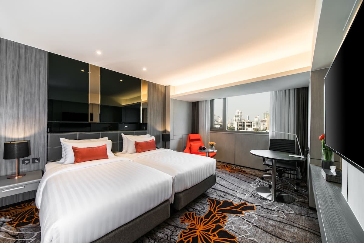 Ein Hotelzimmer mit einem großen Bett, einem Schreibtisch, einem Sessel, einem Fernseher und Blick auf die Stadt.