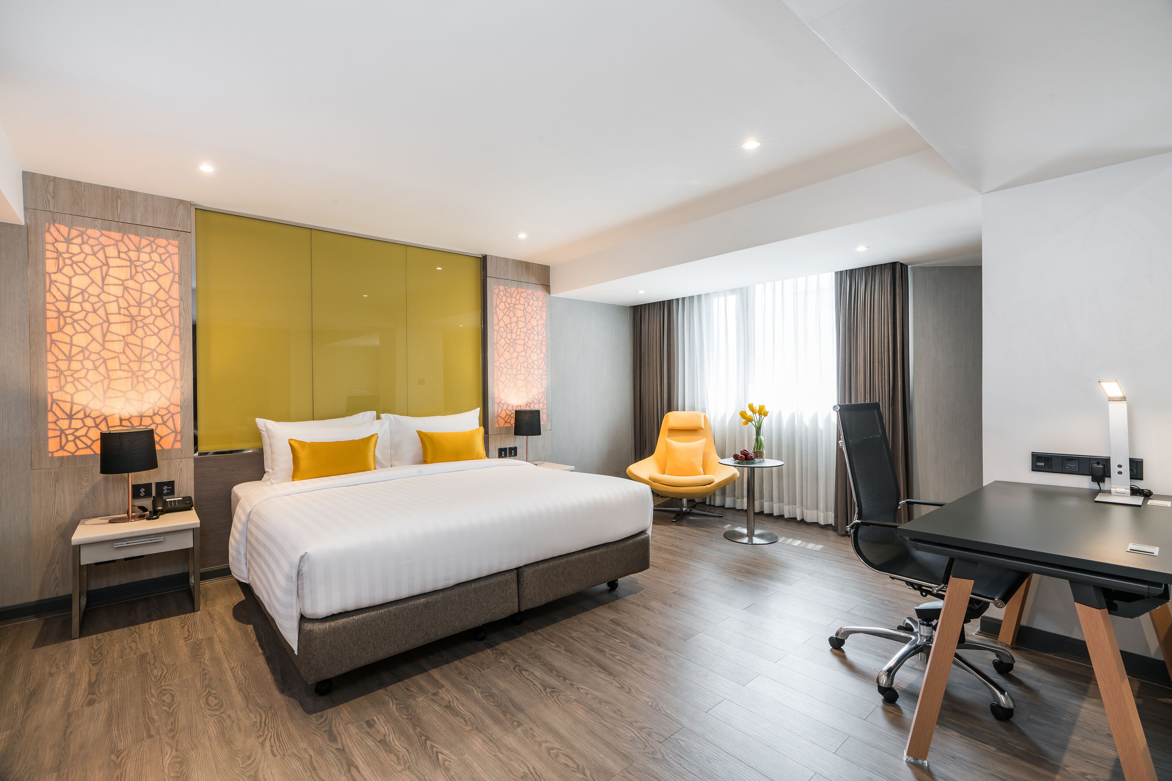 A modern hotel room with a large bed, a desk, a chair, and a small table with flowers.