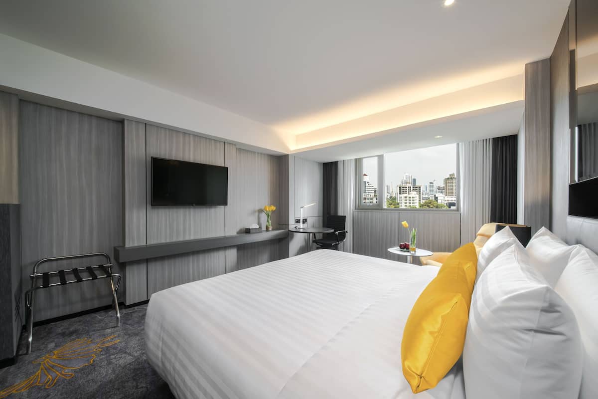 Ein modernes Hotelzimmer mit einem großen Bett, einem Schreibtisch, einem Flachbildfernseher und Blick auf die Stadt.