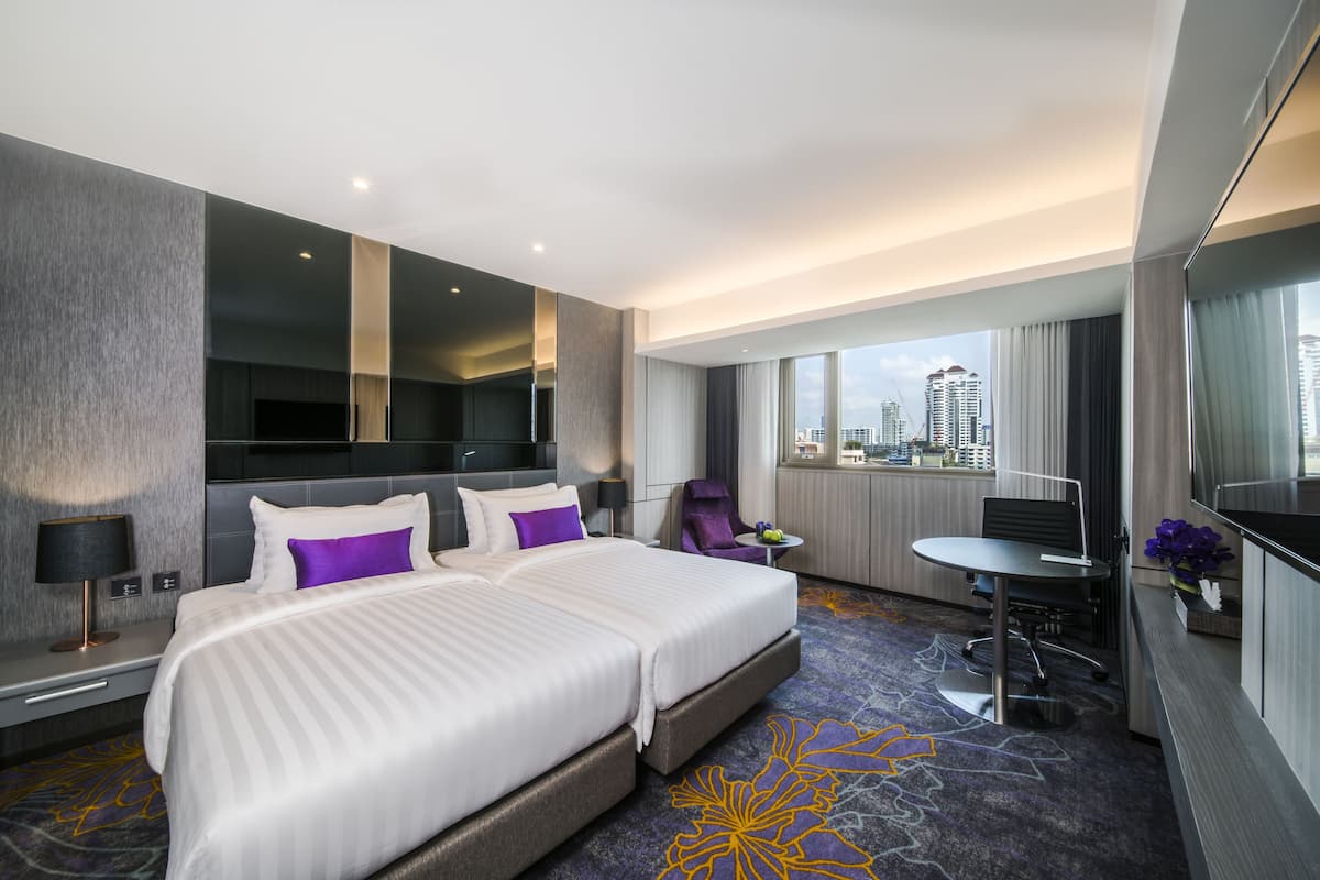 Ein Hotelzimmer mit einem großen Bett, einem Schreibtisch, einem Sessel und Blick auf die Stadt.