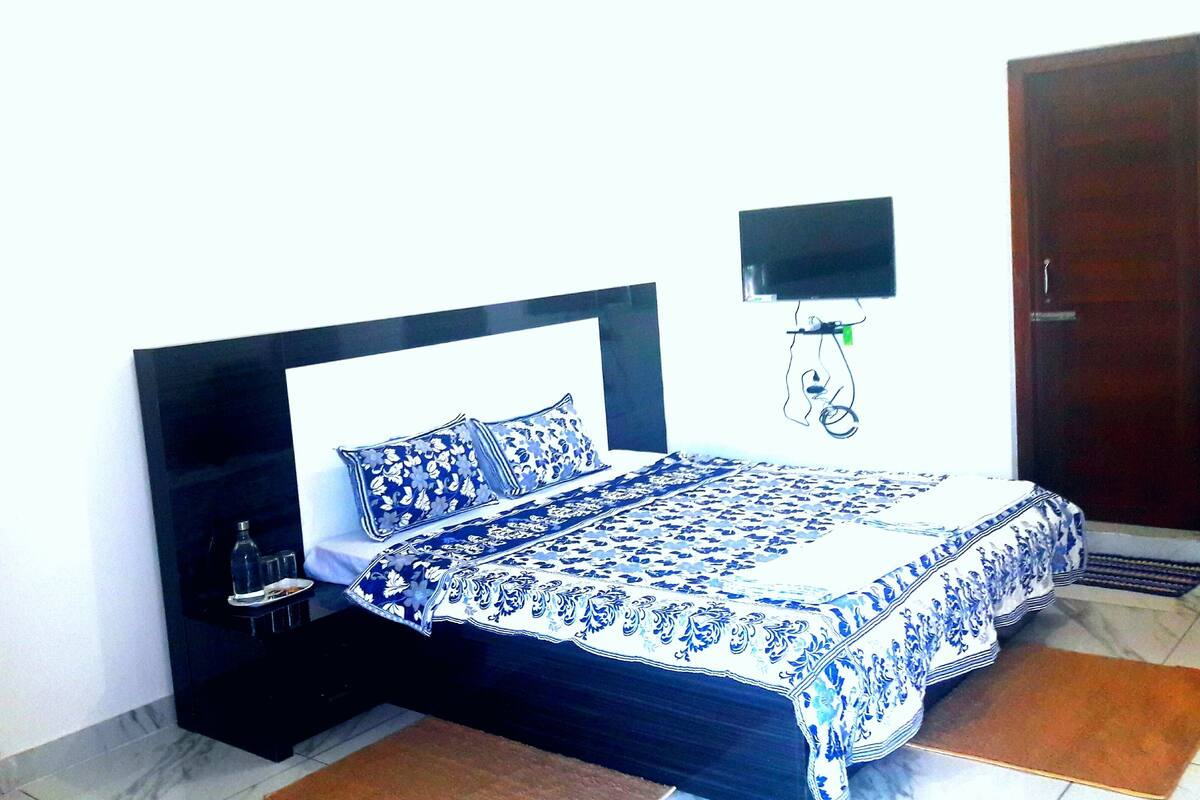 Quarto com cama, mesa de cabeceira, televisão na parede e uma porta.
