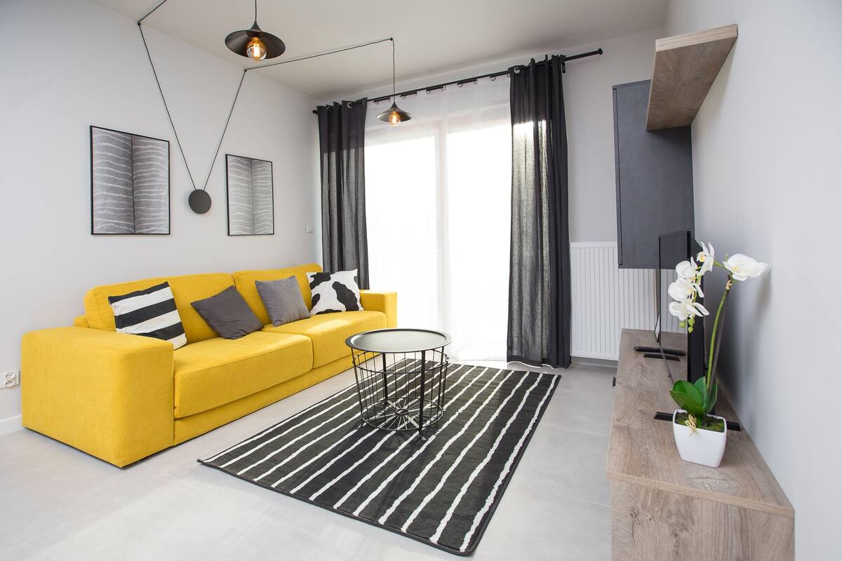 A modern living room with a yellow sofa, a round coffee table, a black and white striped rug, and a potted orchid.
