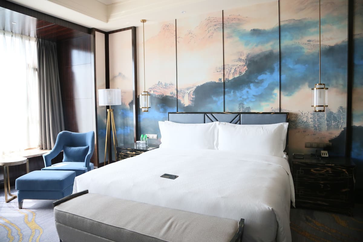 Une chambre d’hôtel avec un grand lit, un bureau avec une lampe, une chaise et un tableau au mur.