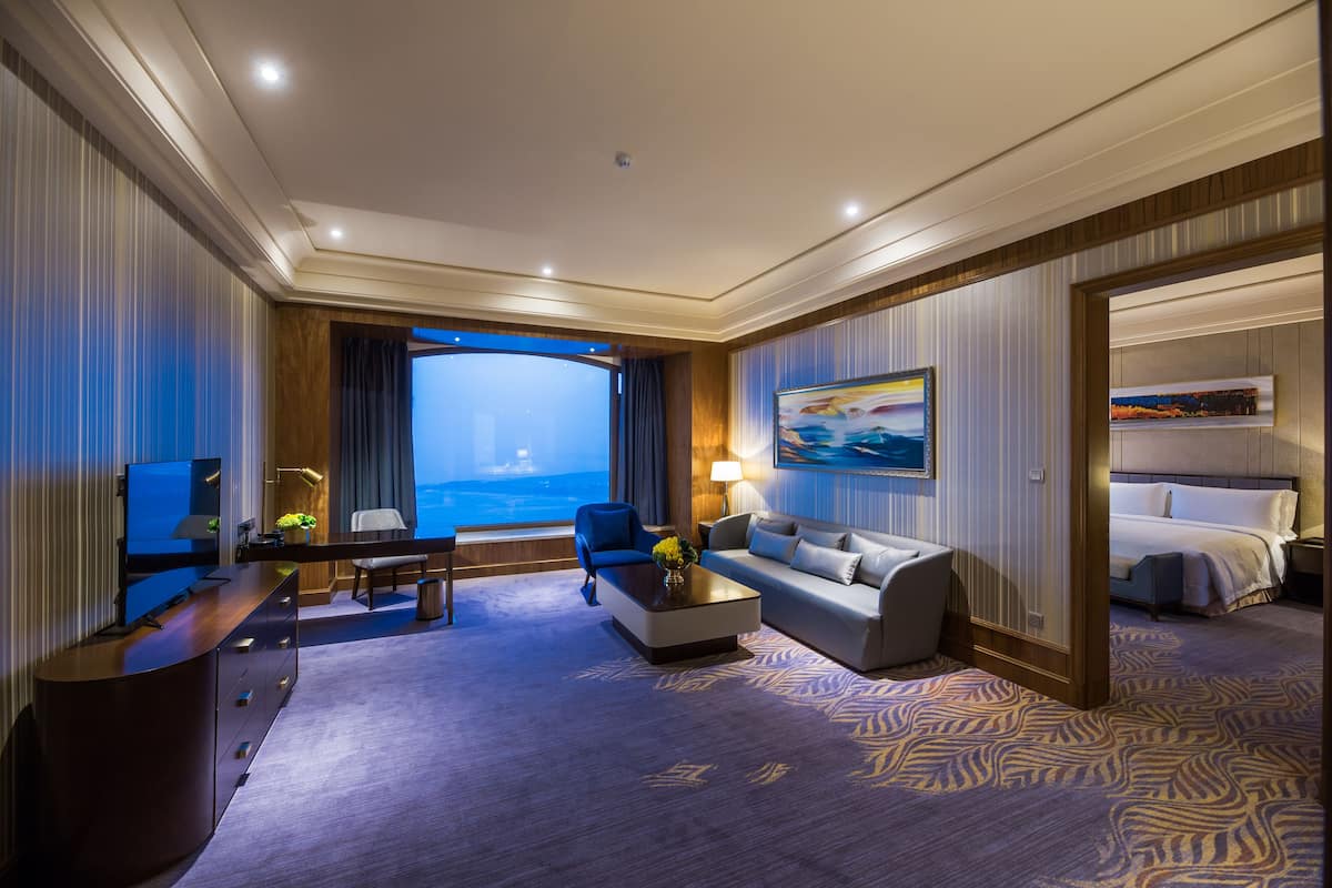 Une chambre d’hôtel moderne dotée d’une grande fenêtre, d’un canapé, d’une table basse, d’un téléviseur et d’un lit.